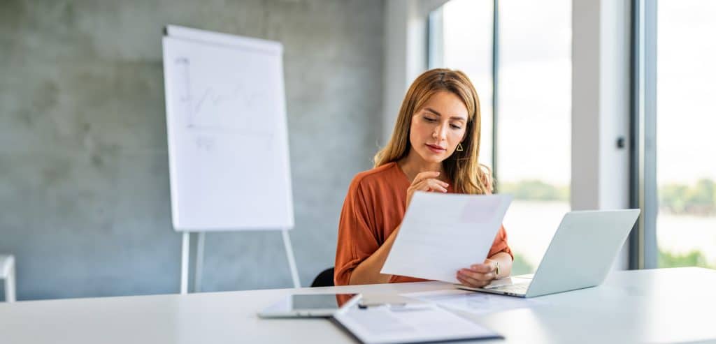 FAQs 1 - Accredo Woman in front of laptop looking at a piece of paper